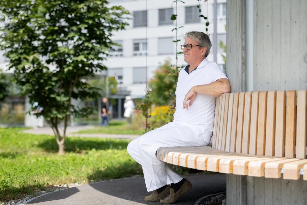 Vital Schreiber blickt in die Zukunft: Für ihn kann diese nur aus einem regionalen Spitalverbund bestehen. Ein Mann in weisser Kleidung sitzt in einem Park auf einer Bank.